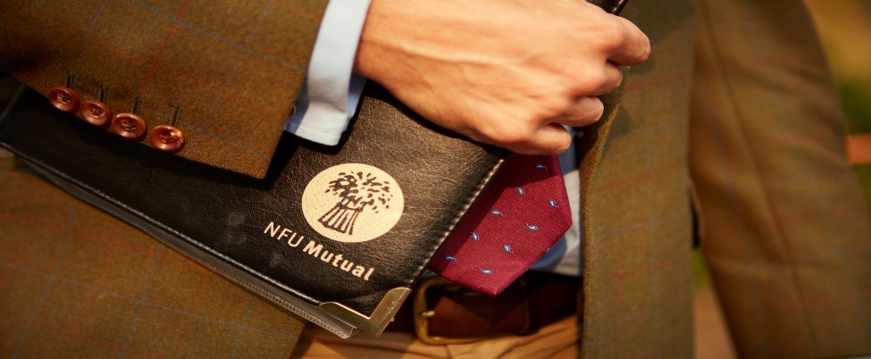 Person in a tweed jacket holding a black NFU Mutual folder against a red patterned tie.