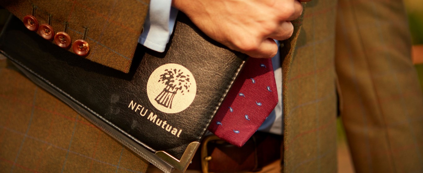 Person in a tweed jacket holding a black NFU Mutual folder against a red patterned tie.