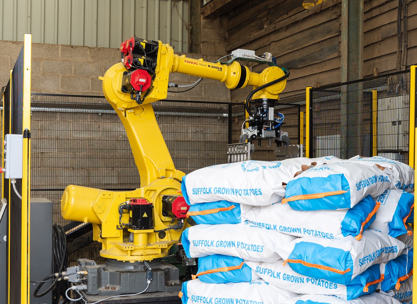 Yellow robotic arm stacking bags labelled ‘Suffolk Grown Potatoes’ inside an industrial shed.