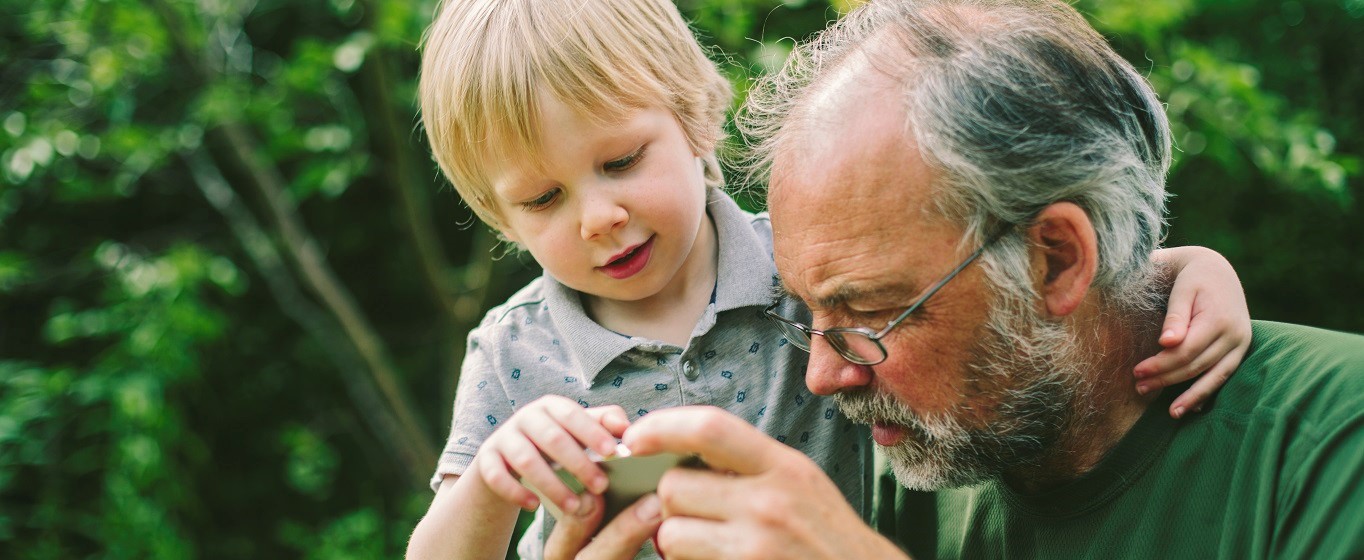 Grandfather and grandson looking closely at something they are both holding.