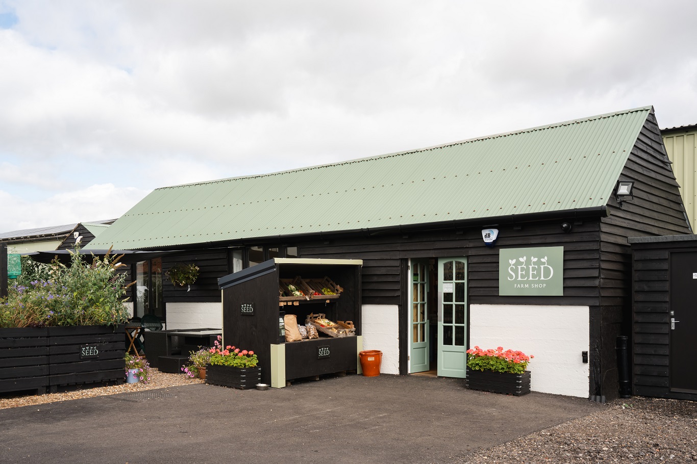 SEED farm shop building with a pale green roof and door, displaying fresh produce and plants outside.
