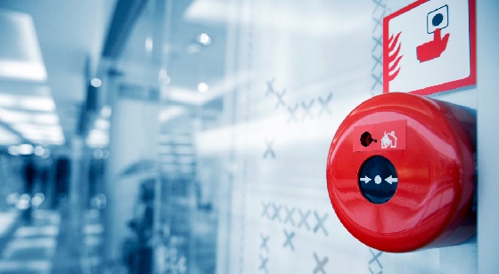 Red emergency fire alarm button installed on a glass wall in an office hallway