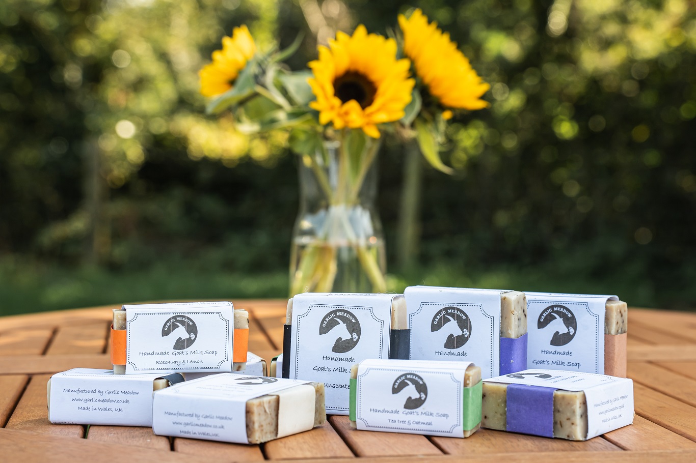 Handmade goat’s milk soaps on a wooden table with sunflowers in the background