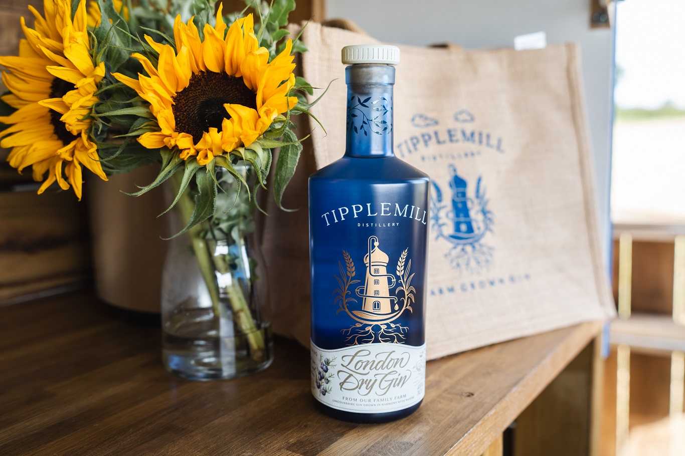 Bottle of Tipplemill London Dry Gin beside a vase of sunflowers