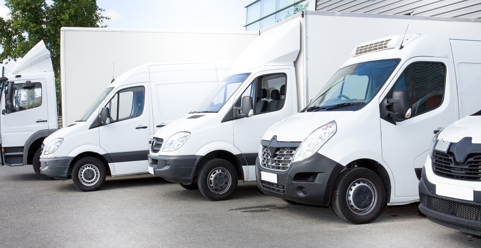 Row of white commercial vans parked side by side in a forecourt.