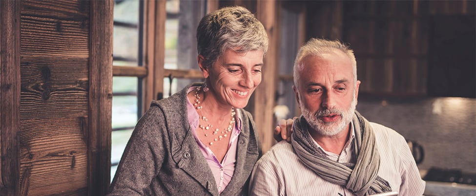 Two people sitting closely together indoors, one with an arm around the other, in a warm wooden room.