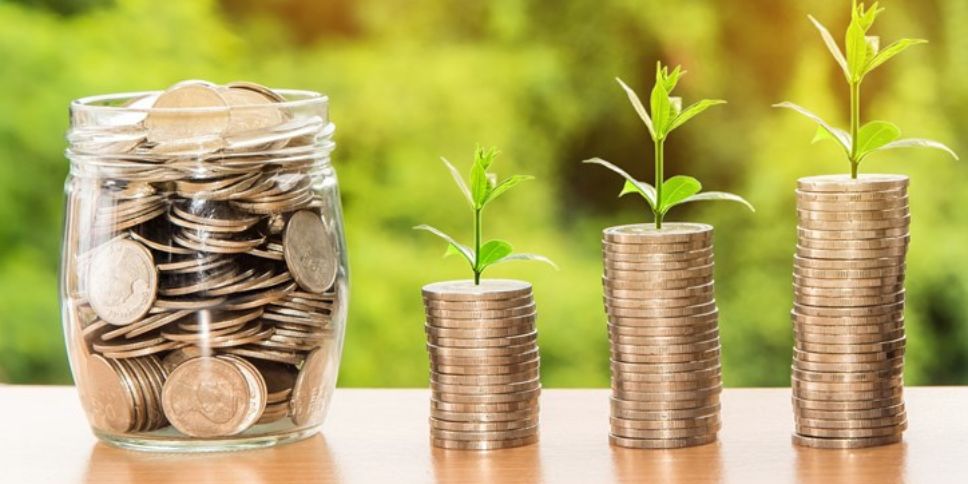 Coin jar next to three coin stacks with small sprouts growing from them