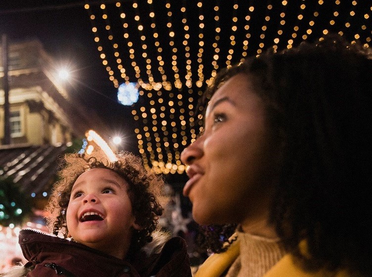 Adult and young child looking up at festive lights strung overhead at night