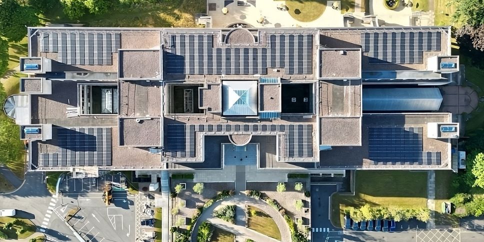 Overhead view of the NFU Mutual Head Office building with a symmetrical layout and rooftop solar panels, surrounded by roads, parking areas, and landscaped grounds.