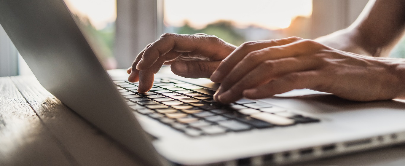 Hands typing on a laptop keyboard near a bright window.