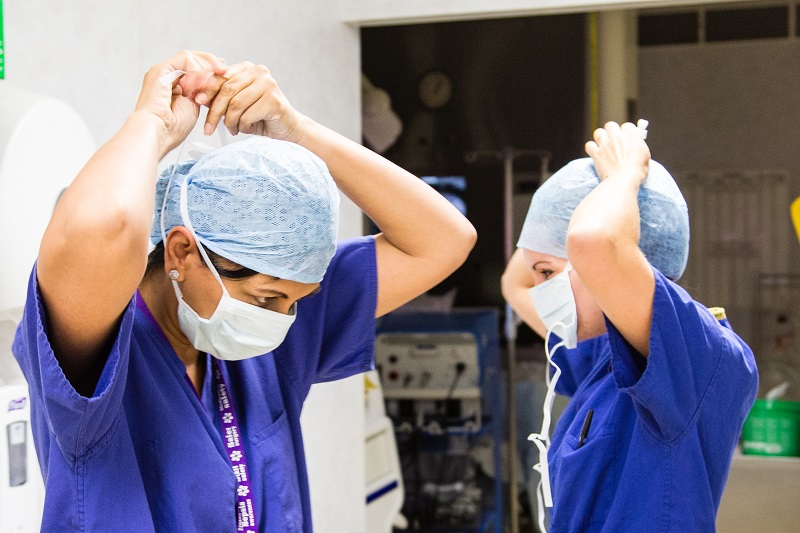 Two healthcare workers in scrubs adjusting surgical caps and masks